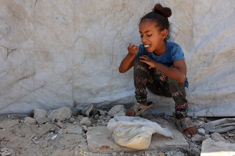 Seorang anak Palestina memakan nasi yang sudah dimasak dengan tangannya setelah menerimanya dari dapur amal di Kota Gaza Sabtu (23/08/2025).