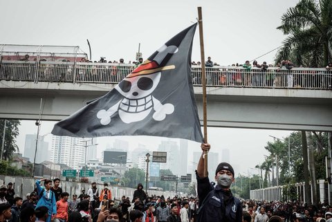 Seorang pengunjuk rasa mengibarkan bendera anime Jepang One saat demo menuntut pembubaran DPR didepan Gedung DPR/ MPR, Jakarta, Senin (25/08/2025).