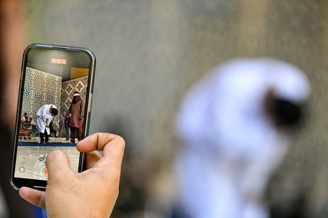 Seorang pria menggunakan ponselnya untuk merekam video seorang pria yang terbukti melakukan hubungan seks sesama dicambuk di depan umum oleh seorang anggota polisi Syariah di Banda Aceh,  Selasa (26/08/2025).