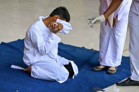 Seorang pria  menangis saat menjalani hukuman cambuk di depan umum oleh anggota polisi syariat di Banda Aceh, Selasa (26/08/2025).