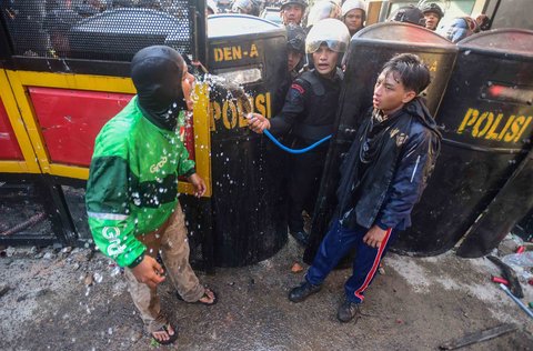 Anggota Brimob mengucurkan air ke pengunjuk rasa untuk mengurangi rasa perih akibat gas air mata  di Mako Brimob, Kwitang, jakarta, Jumat (29/08/2025).