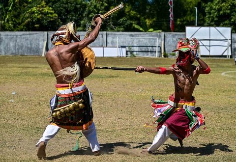 Para pria Manggarai bernyanyi dan menari saat mengikuti Caci yaitu ritual adu cambuk  di Stadion Galing Surabaya, Minggu (03/08/2025).