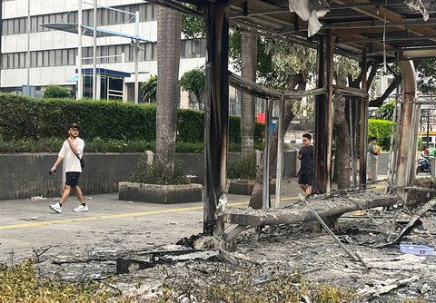 Pejalan kaki melewati halte yang hangus terbakar di Jalan Sudirman, Jakarta,  Sabtu (30/8/2025).