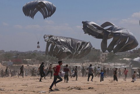 Warga Palestina berlari untuk  mengambil bantuan kemanusiaan yang dijatuhkan dengan parasut ke Zawaida di Jalur Gaza tengah, Senin (04/08/2025).
