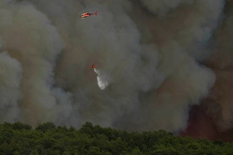 Helikopter keamanan sipil menjatuhkan air di atas kebakaran hutan di Jonqui&egrave;res, Prancis barat daya, Selasa (05/08/2025) waktu setempat.