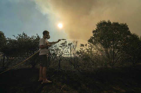 Seorang warga menyemprot air di depan hutan belantara di Tournissan, Prancis barat daya, Selasa (05/08/2025) waktu setempat.