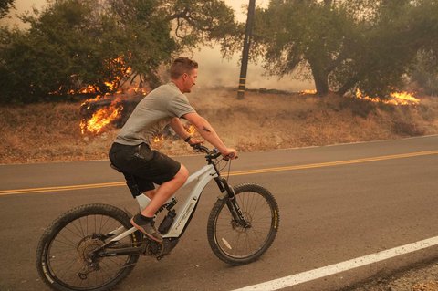 Seorang warga bersepeda di sepanjang Jalan Halsey Canyon saat kebakaran hutan  di Halsey Canyon, California,  AS, Kamis (07/08/2025).