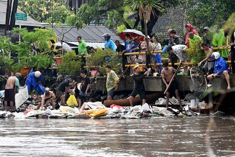 Warga membersihkan puing-puing yang tersangkut di jembatan akibat hujan deras di Denpasar, Bali, Rabu (10/09/2025).