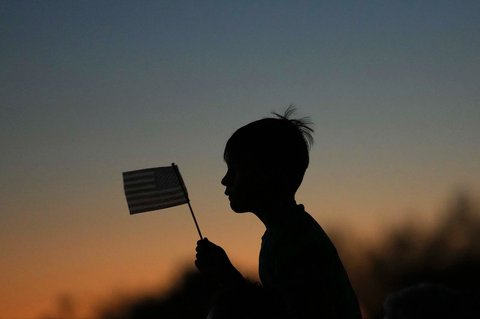 Seorang anak memegang bendera AS saat kegiatan  doa untuk Charlie Kirk  di Scottsdale, Arizona, Rabu (10/09/2025).
