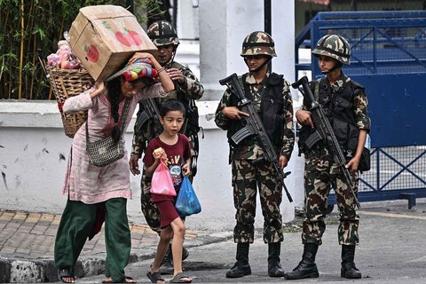 Warga membawa buah-buahan melewati personel militer di luar Istana Presiden Nepal saat pemberlakuan jam malam di Kathmandu, Nepal, Jumat (12/9/2025).