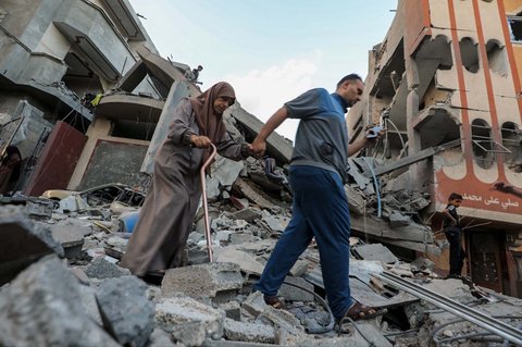 Seorang pria dan seorang wanita Palestina berjalan di atas reruntuhan bangunan yang terkena serangan Israel di kamp pengungsi Nuseirat di Jalur Gaza tengah, Kamis (25/09/2025).