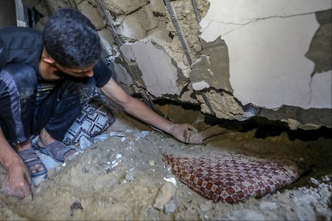 Pemuda Palestina menyentuh tangan seorang anak yang terkubur di bawah reruntuhan bangunan yang terkena serangan Israel di kamp pengungsi Nuseirat di Jalur Gaza tengah, , Kamis (25/09/2025).