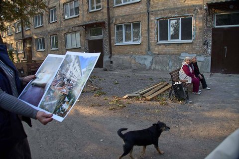 Pejabat setempat menunjukkan foto kerusakan bangunan akibat pertempuran Rusia&ndash;Ukraina kepada wartawan, sementara warga duduk di dekat apartemen yang baru direnovasi di Avdiivka, Donetsk, Ukraina, Sabtu (27/9/2025). Kota ini kini berada di bawah kendali Rusia.