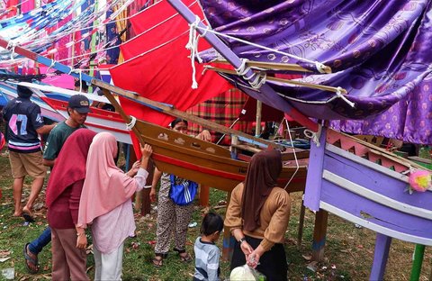Warga menunggu makanan dan beragam peralatan rumah tangga tangga  yang akan dibagikan dari  miniatur perahu Pinisi di Desa Damai, Sulawesi Selatan, Minggu (07/09/2025).