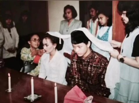 Sementara itu, Santi tampil memikat dalam balutan kebaya putih dengan detail bordir halus. Siluet kebaya yang ringan berpadu dengan kain bernuansa lembut, menghadirkan tampilan pengantin yang