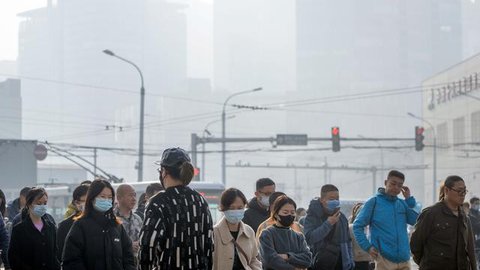 Komuter yang memakai masker berjalan melintasi persimpangan di kawasan pusat bisnis pada hari dengan tingkat polusi udara yang tinggi di Beijing, China, Senin (6/3/2023). Pejabat ekonomi Chin