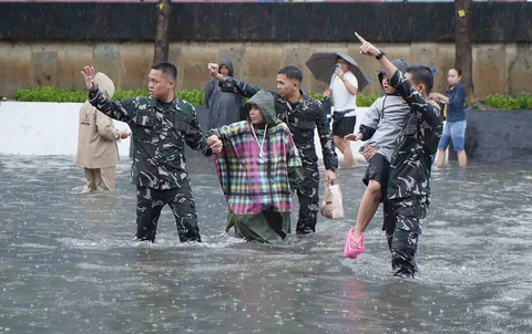 Prajurit TNI Angkatan Laut membantu warga melintasi banjir di Jalan Raya Pademangan, Jakarta Utara. Senin (12/01/2026)