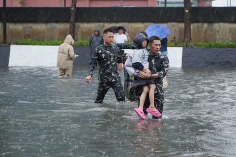 Prajurit TNI Angkatan Laut membantu warga melintasi banjir di Jalan Raya Pademangan, Jakarta Utara. Senin (12/01/2026)