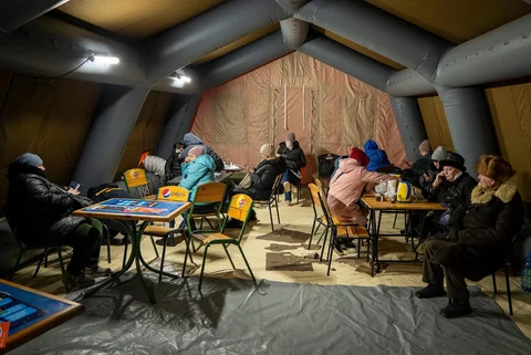 Warga menghangatkan diri di tenda darurat yang disediakan bagi warga setelah serangan udara Rusia terhadap fasilitas energi, yang menyebabkan pemadaman listrik, air, dan pemanas di tengah musim dingin di Kyiv, Ukraina, Selasa (13/01/2026).