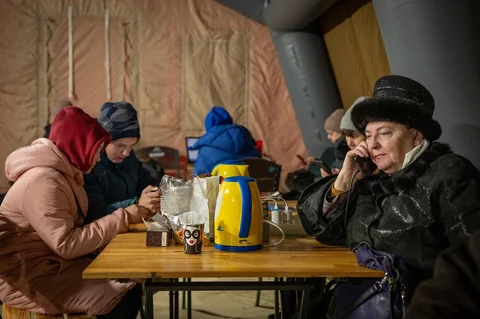 Warga menghangatkan diri di tenda darurat yang disediakan bagi warga setelah serangan udara Rusia terhadap fasilitas energi, yang menyebabkan pemadaman listrik, air, dan pemanas di tengah musim dingin di Kyiv, Ukraina, Selasa (13/01/2026).