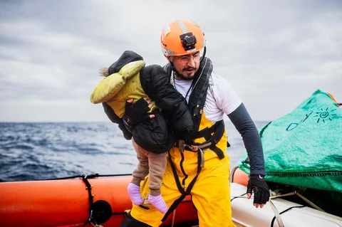 Seorang anggota kru kapal penyelamat &ldquo;Ocean Viking&rdquo; menggendong seorang anak kecil di atas perahu karet (RHIB) mereka selama operasi penyelamatan di zona pencarian dan penyelamatan di lepas perairan internasional Libya, Jumat (16/01/2026).