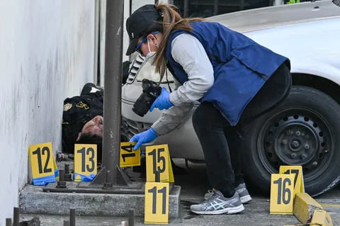 Seorang jaksa Kementerian Publik mengumpulkan barang bukti di dekat jenazah seorang polisi yang dibunuh oleh anggota geng di lingkungan Castanas, Villa Nueva, Guatemala, Minggu, (18/01/2026).