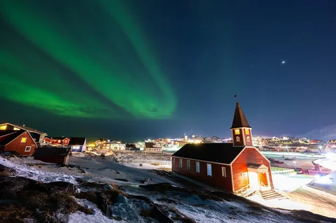 Aurora borealis menerangi langit malam di atas rumah-rumah penduduk di Nuuk, Greenland, Jumat (23/01/2026) waktu setempat.