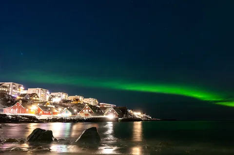 Aurora borealis menerangi langit malam di atas rumah-rumah penduduk di Nuuk, Greenland, Jumat (23/01/2026) waktu setempat.