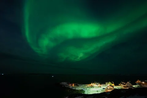 Aurora borealis menerangi langit malam di atas rumah-rumah penduduk di Nuuk, Greenland, Jumat (23/01/2026) waktu setempat.