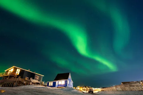 Aurora borealis menerangi langit malam di atas rumah-rumah penduduk di Nuuk, Greenland, Jumat (23/01/2026) waktu setempat.