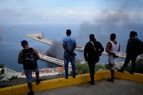 Warga mengamati asap yang mengepul dari dermaga setelah ledakan terdengar di pelabuhan La Guaira, Venezuela, Sabtu (03/0/2026) waktu setempat.