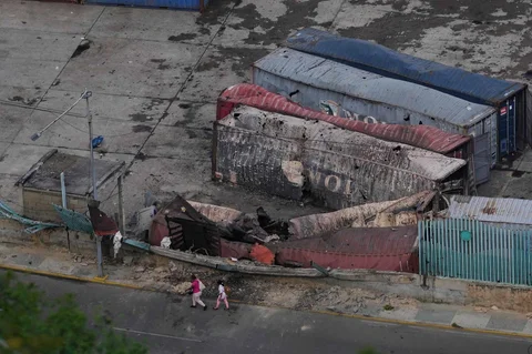 Para pejalan kaki melewati kontainer-kontainer yang hancur di pelabuhan La Guaira setelah ledakan terdengar di Venezuela, Sabtu (03/0/2026) waktu setempat.