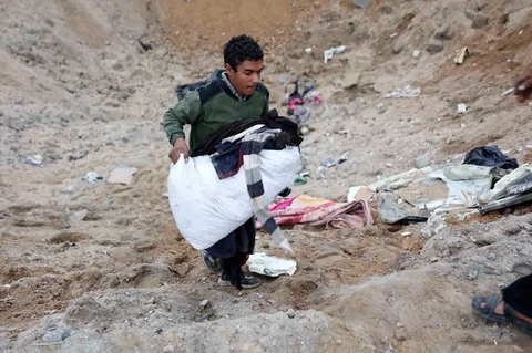 Seorang pria Palestina membawa sekantong pakaian dari kawah setelah militer Israel menembaki kamp tenda yang menampung keluarga pengungsi, di kamp pengungsi Al-Shati, di Kota Gaza, Palestina,  Jumat (09/01/2026).