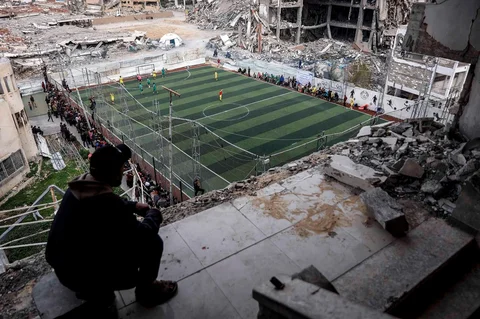 Warga Palestina menyaksikan pertandingan sepak bola lima lawan lima di tengah reruntuhan bangunan yang hancur di Kota Gaz, Senin (09/02/2026) waktu setempat.