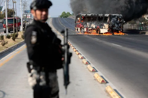 Seorang anggota Kejaksaan berjaga di dekat bus yang dibakar oleh kelompok kejahatan terorganisir sebagai bentuk perlawanan terhadap operasi penangkapan pemimpin Kartel Generasi Baru Jalisco, Nemesio Oseguera di Zapopan, Jalisco, Meksiko, Minggu (22/02/2026).