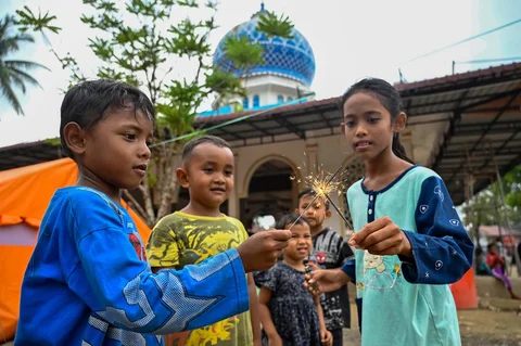 Anak-anak bermain kembang api  samnil menunggu waktu berbuka puasa di dekat tenda-tenda yang didirikan untuk para korban banjir di kompleks sebuah masjid di Meurah Dua, distrik Pidie Jaya, provinsi Aceh, Sabtu (21/02/2026).
