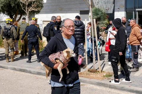 Seorang pria berjalan sambil menggendong anjing saat evakuasi penghuni  gedung yang terkena proyektil di kota Tirat Carmel, Israel utara, selatan Haifa, Sabtu (28/02/2026).