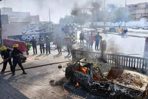 Petugas pemadam kebakaran menyiramkan air ke mobil yang dibakar oleh para demonstran di dekat Konsulat AS di Karachi, Pakistan, Minggu, (01/03/2026).