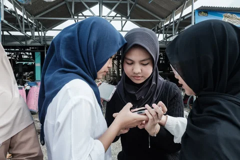 Anak-anak  berusia 15 tahun menggunakan ponsel pintar mereka di jalanan Jakarta,  (26/03/2026).