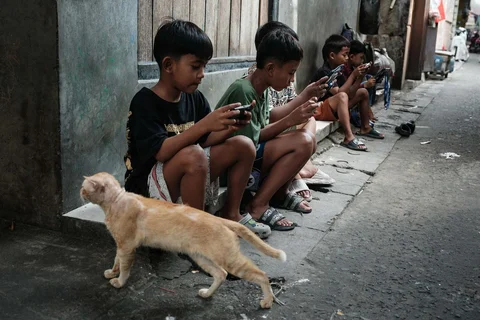 Anak-anak bermain game online satu sama lain di ponsel pintar dan tablet di sepanjang gang di Jakarta, (26/03/2026).