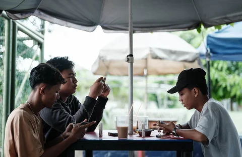Anak laki-laki berusia 16 tahun bermain game online melawan teman-temannya di ponsel pintarnya di samping lapangan tenis di Jakarta, (26/03/2026).