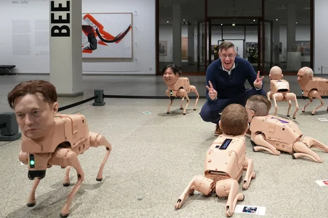 Seniman Beeple, Mike Winkelmann, berpose di dalam instalasinya yang berjudul Regular Animals, dengan robot-robot yang menyerupai Elon Musk (kiri), Kim Jong Un (kedua dari kiri), dan Pablo Picasso (kanan), di museum Neue Nationalgalerie di Berlin, Jerman, Selasa, (28/04/2026).