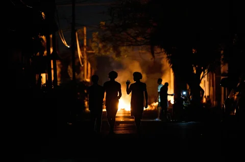 Orang-orang berjalan di jalan di samping api unggun yang dinyalakan oleh warga sebagai bentuk protes terhadap pemadaman listrik berkepanjangan di jalanan Havana, Kuba, Kamis malam (14/05/2026).