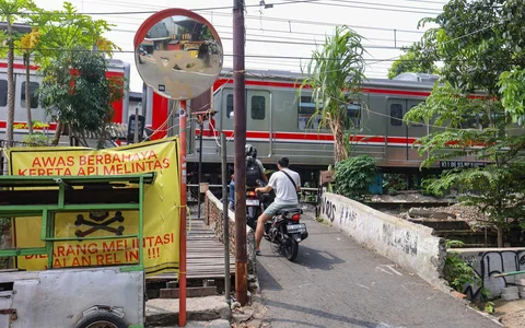 Pengendara melintas di samping spanduk peringatan dan larangan melintas di perlintasan liar jalur kereta api di kawasan Tebet, Jakarta, Jumat(15/05/2026).