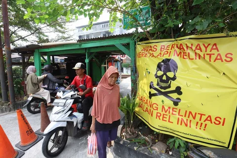 Pengendara melintas di samping spanduk peringatan dan larangan melintas di perlintasan liar jalur kereta api di kawasan Tebet, Jakarta, Jumat(15/05/2026).