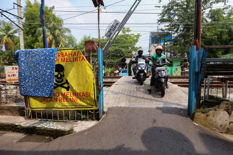 Pengendara melintas di samping spanduk peringatan dan larangan melintas di perlintasan liar jalur kereta api di kawasan Tebet, Jakarta, Jumat(15/05/2026).