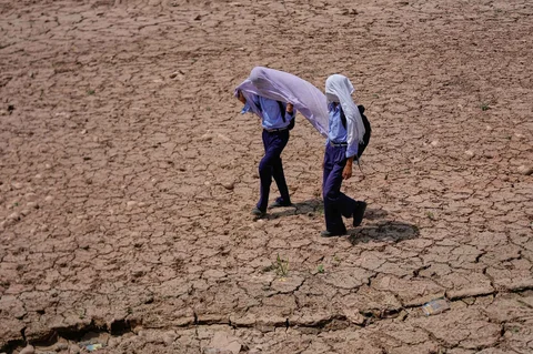 Anak-anak sekolah menggunakan handuk katun di atas kepala ntuk melindungi diri dari terik matahari siang saat mereka berjalan melintasi ladang kering di pinggiran Jammu, India, Rabu (20/05/2026)