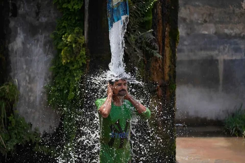 Seorang pria mandi menggunakan keran air pinggir jalan untuk mendinginkan diri di hari yang panas di pinggiran Jammu, India, Selasa, (19/05/2026).