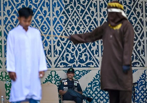 Seorang anggota polisi Syariah menyaksikan seorang pria (kiri) menerima 100 cambukan selama hukuman cambuk di depan umum di Taman Bustanussalatin, Banda Aceh, Aceh, Kamis (21/5/2026).