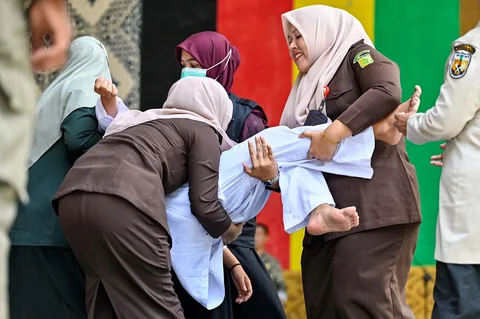 Polisi syariah dan petugas hukum membawa seorang wanita yang pingsan setelah dicambuk di depan umum di  Taman Bustanussalatin, Banda Aceh, Aceh, Kamis (21/5/2026).